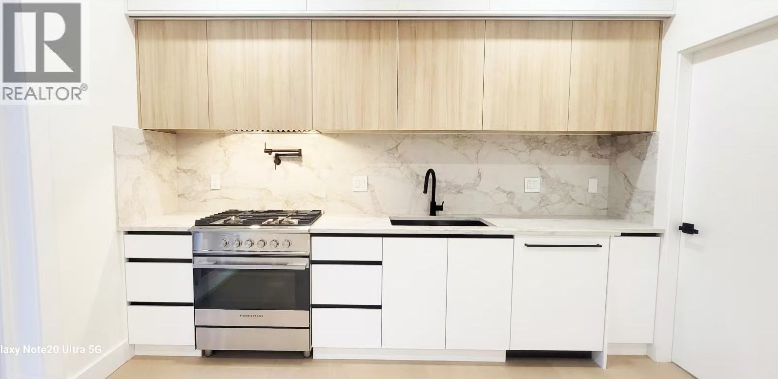 Kitchen with wood-grain uppers, marble-look slab backsplash and gas range